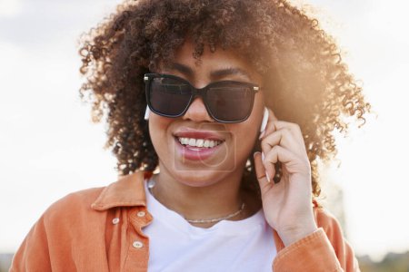 Foto de Primer plano de mujer negra alegre en gafas de sol y auriculares - Imagen libre de derechos