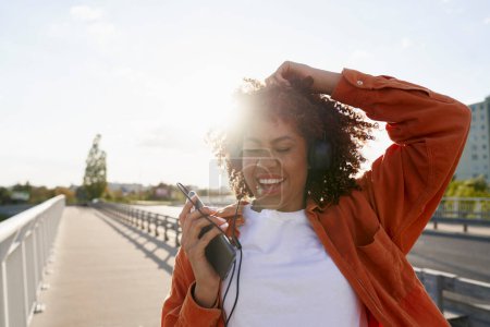 Téléchargez les photos : Gros plan de la femme noire portant des écouteurs et dansant sur le pont - en image libre de droit