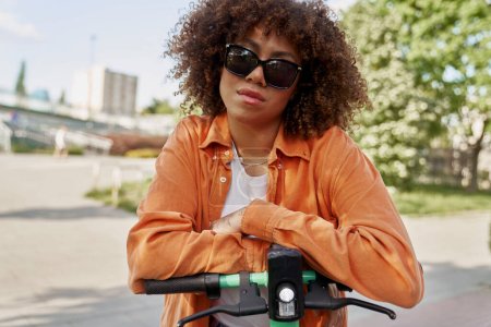 Photo for Front view of black woman in sunglasses riding an electric scooter - Royalty Free Image