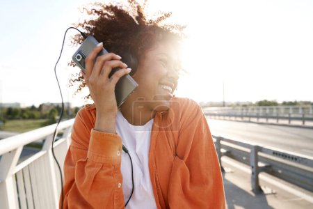 Photo for Black woman wearing headphones and dancing on the bridge - Royalty Free Image