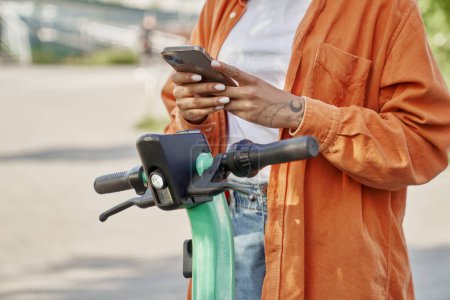 Téléchargez les photos : Femme méconnaissable utilisant un téléphone mobile pour utiliser un scooter électrique - en image libre de droit