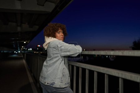 Téléchargez les photos : Femme noire debout sur le pont la nuit et regardant la caméra - en image libre de droit
