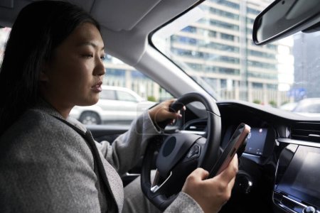 Téléchargez les photos : Femme chinoise utilisant un téléphone portable tout en conduisant une voiture - en image libre de droit