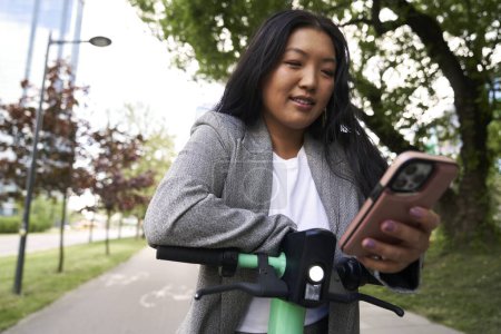 Foto de Mujer china usando teléfono móvil para usar un scooter eléctrico - Imagen libre de derechos