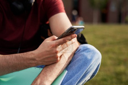 Téléchargez les photos : Téléphone de navigation étudiant méconnaissable tout en étant assis sur le campus - en image libre de droit