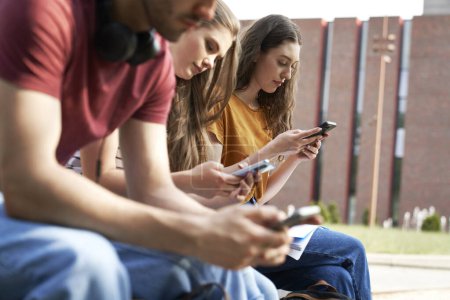 Photo for University students browsing phones next to university campus building - Royalty Free Image