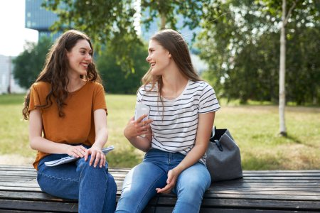 Téléchargez les photos : Deux étudiantes caucasiennes assises à l'extérieur du campus universitaire et bavardant - en image libre de droit