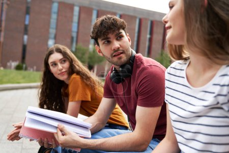 Téléchargez les photos : Groupe de trois étudiants caucasiens qui étudient à l'extérieur du campus universitaire - en image libre de droit