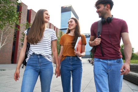 Téléchargez les photos : Vue en angle bas du groupe de trois étudiants caucasiens marchant à travers le campus universitaire - en image libre de droit