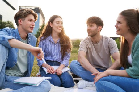 Téléchargez les photos : Groupe d'étudiants caucasiens étudiant à l'extérieur du campus universitaire assis sur l'herbe - en image libre de droit