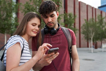 Téléchargez les photos : Deux étudiants naviguant sur le téléphone mobile à côté du campus universitaire - en image libre de droit