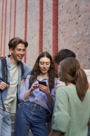 Photo for University students browsing phone next to university campus building - Royalty Free Image