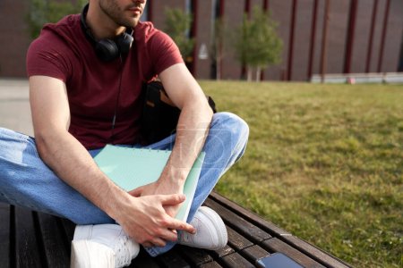 Téléchargez les photos : Étudiant universitaire masculin méconnaissable assis à l'extérieur du campus universitaire - en image libre de droit