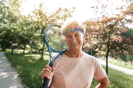 Téléchargez les photos : Portrait de femme âgée debout dans le parc et tenant une raquette de tennis - en image libre de droit