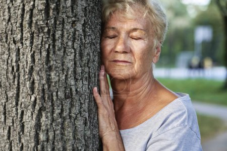 Calm senior woman doing breathing exercise next to the tree in the park