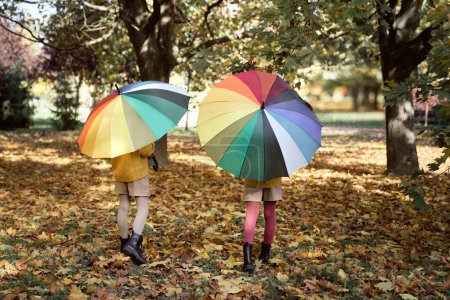 Téléchargez les photos : Vue arrière des sœurs marchant avec un parapluie coloré - en image libre de droit