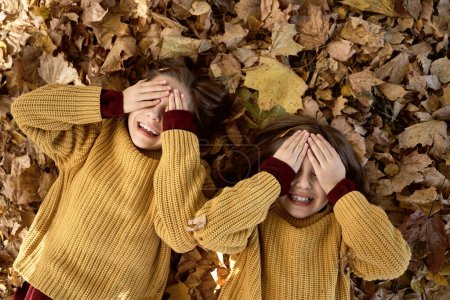 Foto de Dos hermanas tumbadas en el suelo con hojas y ojos tapados - Imagen libre de derechos