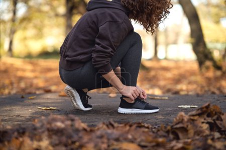 Téléchargez les photos : Femme en vêtements de sport attacher des chaussures avant de faire du jogging dans le parc - en image libre de droit