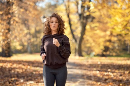 Téléchargez les photos : Femme caucasienne jogging dans le parc en automne par temps ensoleillé - en image libre de droit