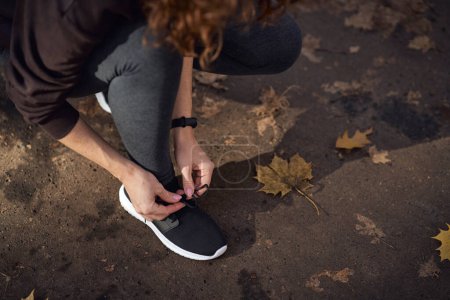 Téléchargez les photos : Vue grand angle de la femme en vêtements de sport attacher des chaussures avant de faire du jogging dans le parc - en image libre de droit