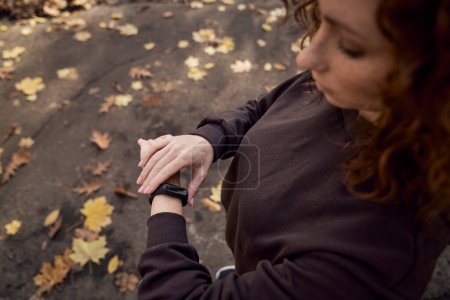 Téléchargez les photos : Vue grand angle de la femme caucasienne en utilisant montre pendant faire du sport dans le parc - en image libre de droit