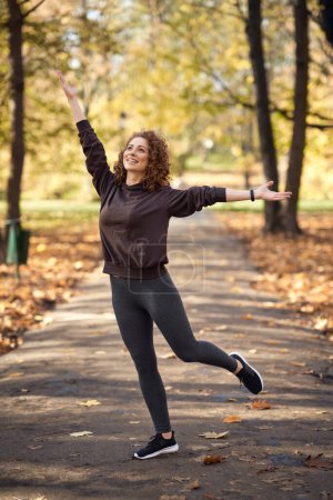 Photo for Wide shot of energetic caucasian woman in the park in the autumn   with arms outstretched - Royalty Free Image