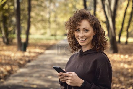 Téléchargez les photos : Portrait de femme caucasienne naviguant sur téléphone mobile avec plaisir pendant l'activité de jogging - en image libre de droit