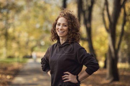 Photo for Portrait of cheerful caucasian woman wearing sports clothes and standing in the autumn park - Royalty Free Image