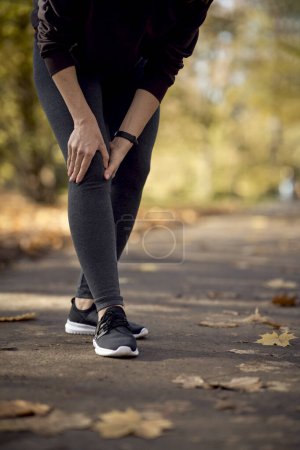 Foto de Sección baja de la mujer que siente lesión en la rodilla durante el trote en el parque - Imagen libre de derechos