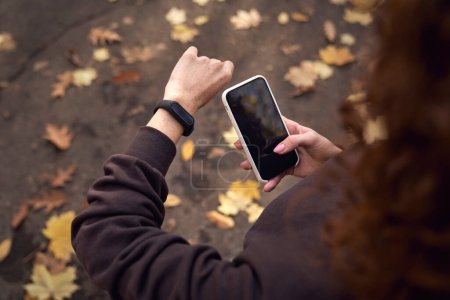 Téléchargez les photos : Vue grand angle de la femme caucasienne en utilisant montre et téléphone portable pendant faire du sport dans le parc - en image libre de droit
