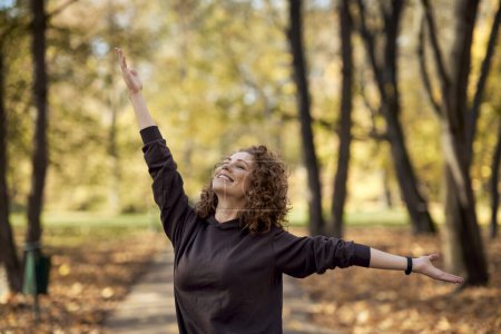 Téléchargez les photos : Femme caucasienne énergique dans le parc à l'automne avec les bras tendus - en image libre de droit
