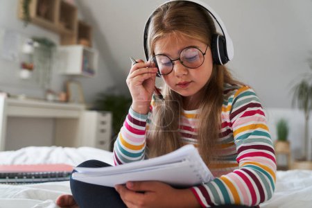 Téléchargez les photos : Caucasienne âge élémentaire fille écouter de la musique tout en étant assis sur le lit - en image libre de droit