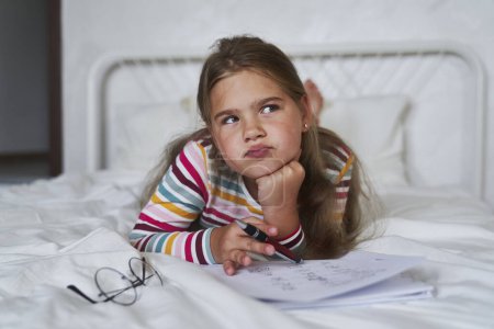 Photo for Thoughtful elementary age studying while leaning on bed - Royalty Free Image