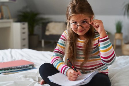 Photo for Portrait of focus elementary age girl studying at the bed - Royalty Free Image