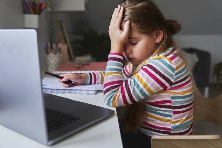 Téléchargez les photos : Fatigué caucasien âge élémentaire fille étudiant sur ordinateur portable - en image libre de droit