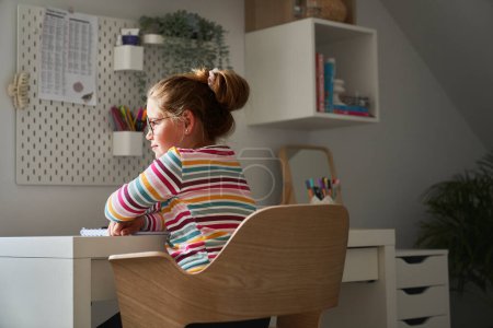 Photo for Elementary age girl studying at the desk and looking away - Royalty Free Image