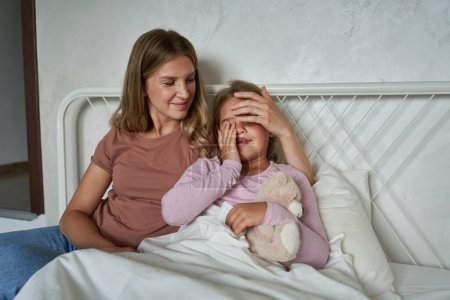 Téléchargez les photos : Mère parlant à sa fille malade enfant couché dans son lit - en image libre de droit