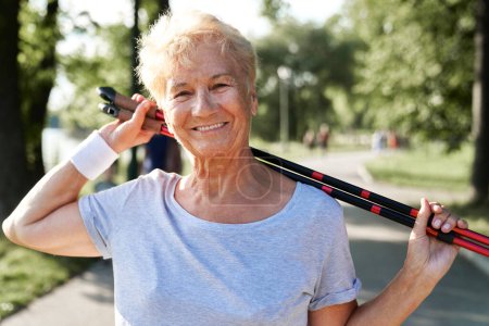 Porträt einer Seniorin mit Nordic-Walking-Stöcken im Park
