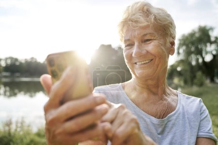 Téléchargez les photos : Femme âgée utilisant un téléphone portable dans le parc - en image libre de droit