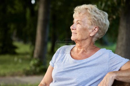 Foto de Mujer mayor sentada en el banco del parque y mirando a su alrededor - Imagen libre de derechos