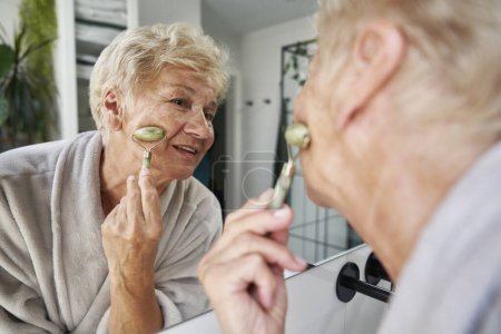 Photo for Senior caucasian woman using face roller in the bathroom - Royalty Free Image