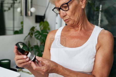 Téléchargez les photos : Femme âgée regardant une bouteille avec du sérum - en image libre de droit