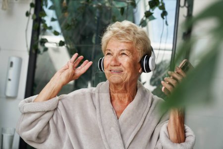 Téléchargez les photos : Femme caucasienne senior utilisant des écouteurs et dansant dans la salle de bain - en image libre de droit