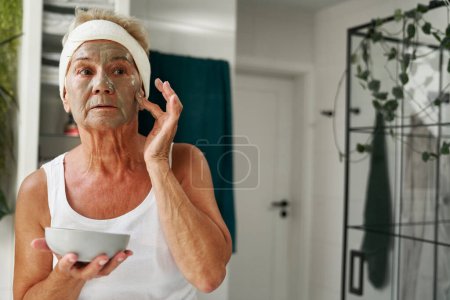 Téléchargez les photos : Femme âgée appliquant masque cosmétique - en image libre de droit