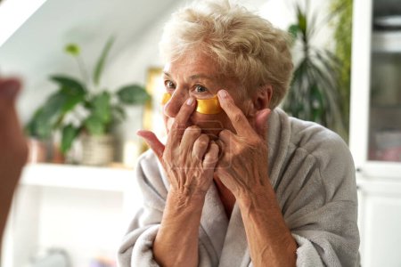 Téléchargez les photos : Femme caucasienne senior appliquant un bandeau oculaire médical dans la salle de bain - en image libre de droit