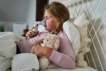 Photo for Elementary age girl  using nebulizer in bed at home - Royalty Free Image