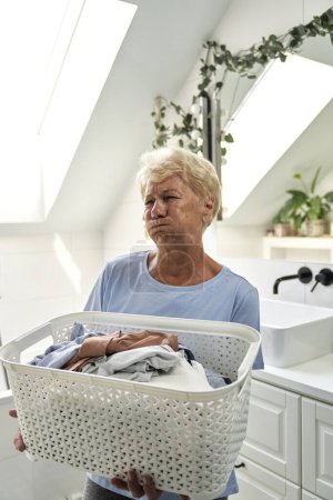 Foto de Cansada mujer caucásica mayor sosteniendo una cesta de lavandería - Imagen libre de derechos