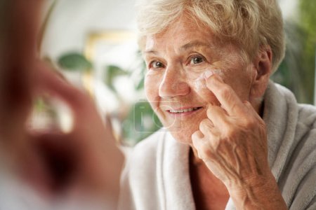 Foto de Mujer mayor aplicando una crema facial - Imagen libre de derechos