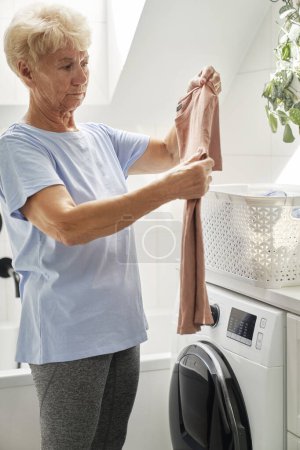 Téléchargez les photos : Femme âgée sur le point de charger une machine à laver - en image libre de droit