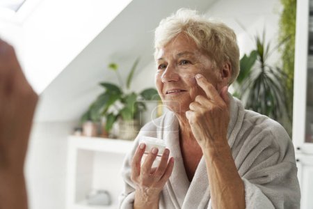 Téléchargez les photos : Femme âgée appliquant une crème pour le visage - en image libre de droit